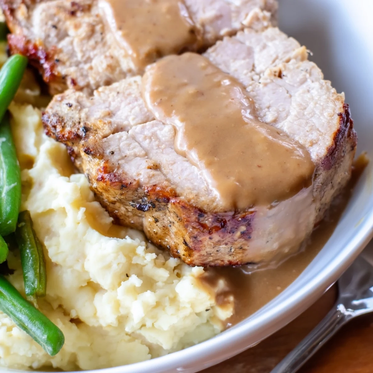 Juicy pork chops on creamy cheddar mash, topped with savory gravy and green beans.  