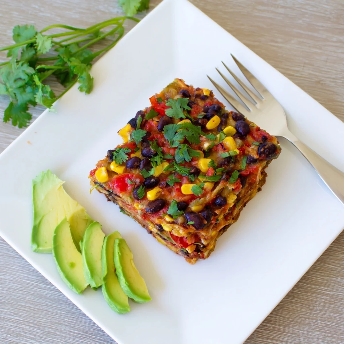 Close-up of a fresh-baked Quick Black Bean and Corn Tortilla Casserole, served with fresh cilantro and avocado.
