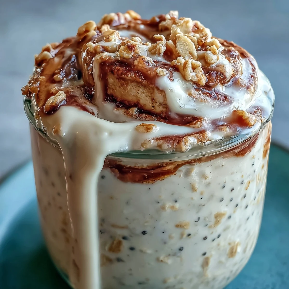 Overnight oats topped with creamy cinnamon roll drizzle and a sprinkle of cinnamon in a jar. 
