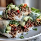 Freshly rolled Thai Basil Beef Rolls served with a spicy dipping sauce on a white plate for lunch.