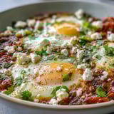 Vibrant shakshuka bowl topped with fresh herbs and crumbled feta, with steam rising from the rich red sauce.