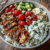 Juicy Greek Chicken Bowls bursting with vibrant vegetables, creamy tzatziki, and hummus.