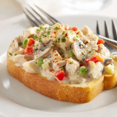 Creamy Chicken à la King atop golden, buttered toast with colorful veggies.