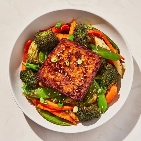 Golden-brown pressed tofu steaks glistening, served atop vibrant stir-fried vegetables and fluffy rice.