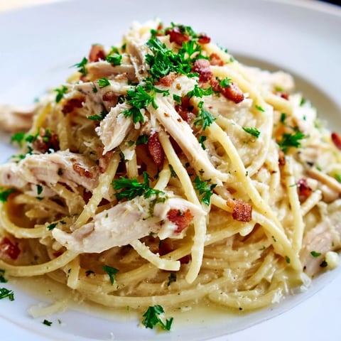 Steam rises from a bowl of Chicken Carbonara, showcasing creamy pasta, crispy bacon, and tender shredded chicken garnished with parsley.