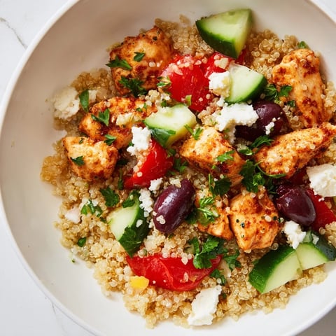 Freshly cooked Mediterranean Chicken Bowl with juicy chicken, feta, olives, chickpeas, cucumber, and quinoa on a white plate.  