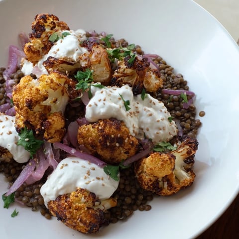 Golden roasted cauliflower florets sit atop a bed of zesty lemon lentil salad, ready for a drizzle of creamy cumin tahini yogurt.