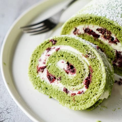 Deliciously rolled matcha sponge cake topped with sweet cranberry whipped cream and powdered sugar.  