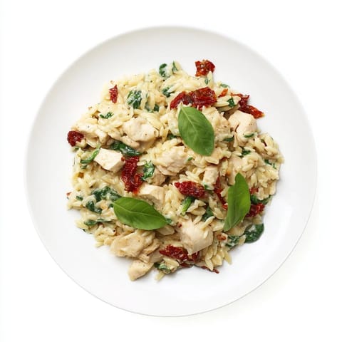 Golden-brown Tuscan Chicken Orzo simmering in a creamy sauce with sun-dried tomatoes, spinach, and fresh basil in a skillet.  