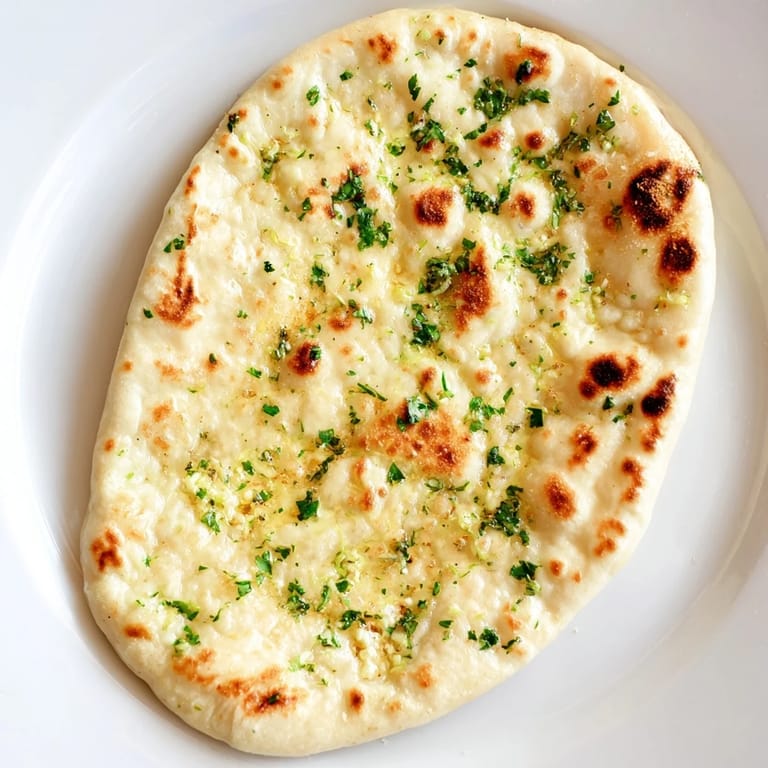 Freshly baked homemade garlic naan, the soft, flavorful Indian flatbread glistening with melted garlic butter.